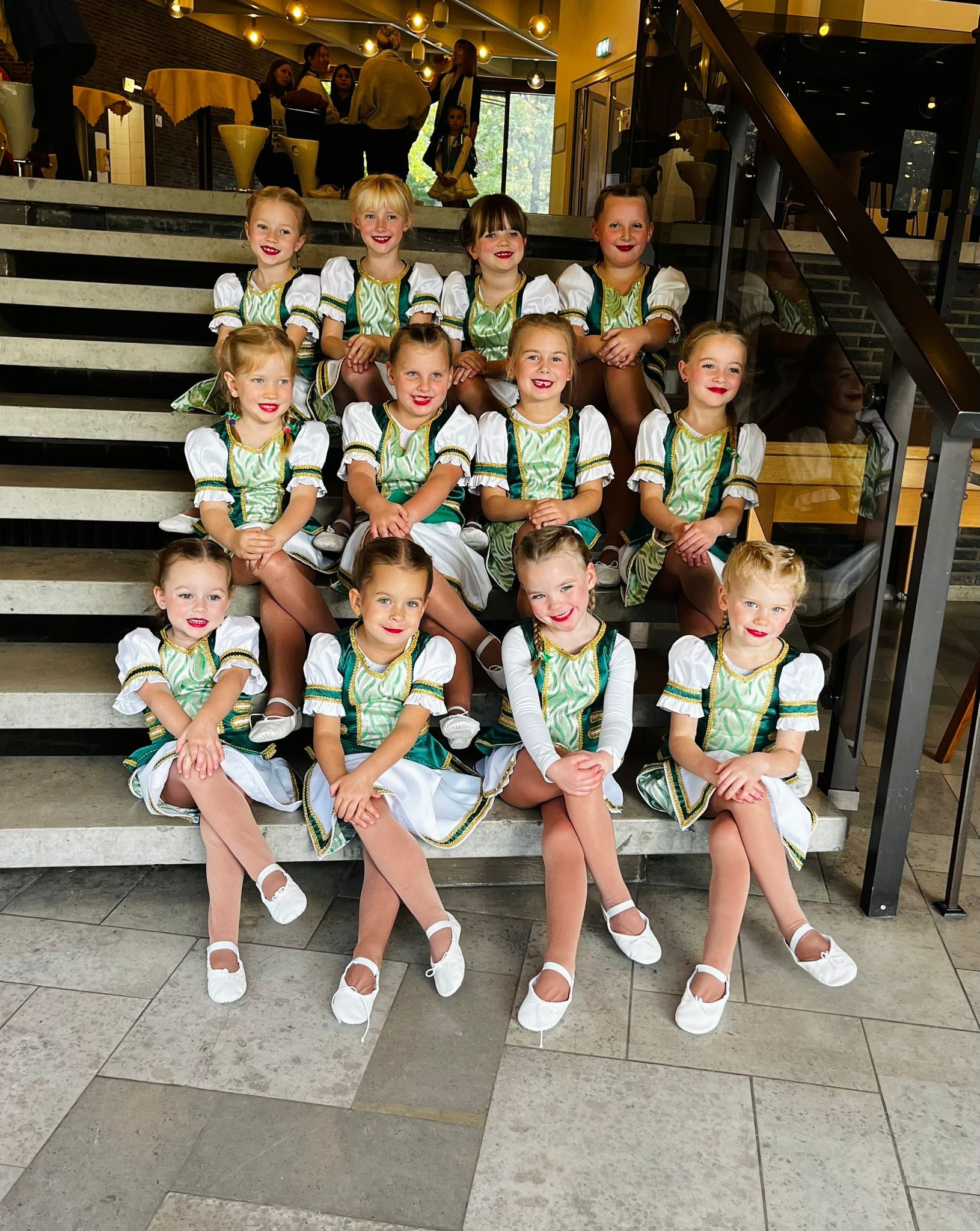 Junge Garde in grün-weißen Uniformen sitzt fröhlich auf einer Treppe, bereit für ihren Auftritt beim Karneval.