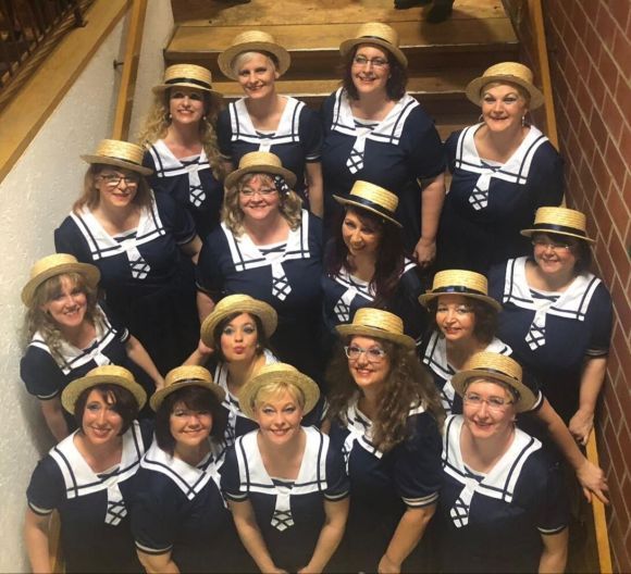 Gruppe Frauen in blauen Matrosenkleidern mit Strohhüten posiert auf Treppe und lächelt in die Kamera.