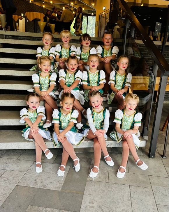 Junge Tänzerinnen der Großen Osterfelder Karnevalsgesellschaft 1906 e.V. sitzen in Uniform fröhlich auf einer Treppe.