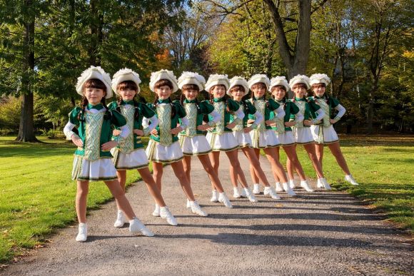 Mädchen in grünen Uniformen posieren im Sonnenschein in Reih und Glied auf einem Weg im Park.