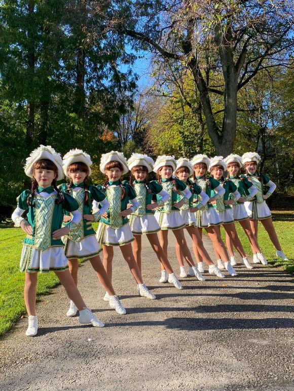 Mädchen in grünen Uniformen posieren im Sonnenschein in Reih und Glied auf einem Weg im Park.